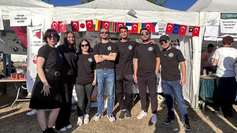 Seven people, dressed in black, in front of a white market stand