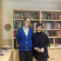 Two people standing side by side in front of wooden bookshelves filled with books and documents in an office at Comillas.