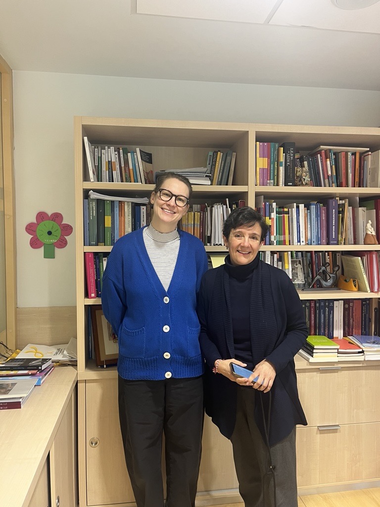 Two people standing side by side in front of wooden bookshelves filled with books and documents in an office at Comillas.