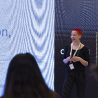 Ana Vucic presenting in front of a large screen displaying text.