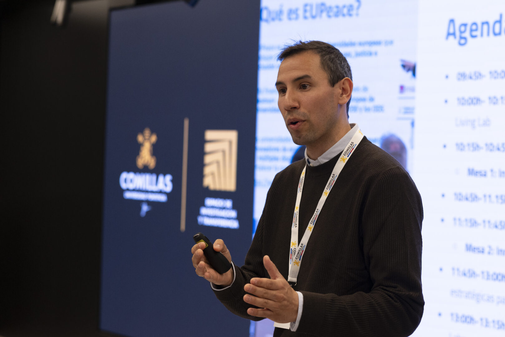 Bernardo Ríos standing and speaking in front of a large screen displaying the Comillas University logo and a presentation agenda.