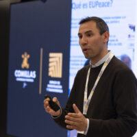 Bernardo Ríos standing and speaking in front of a large screen displaying the Comillas University logo and a presentation agenda.