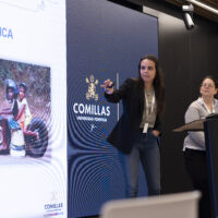 Eva Bajo Marcos and Laura Primo presenting in front of a projected slide showing a photo of two children sitting on a homemade toy vehicle.