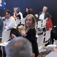 Audience members seated in a conference room, with one attendee in the foreground turning toward the camera.