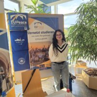 A female student assistant stands at the EUPeace Info booth at the Study Abroad Fair of the University of Marburg.