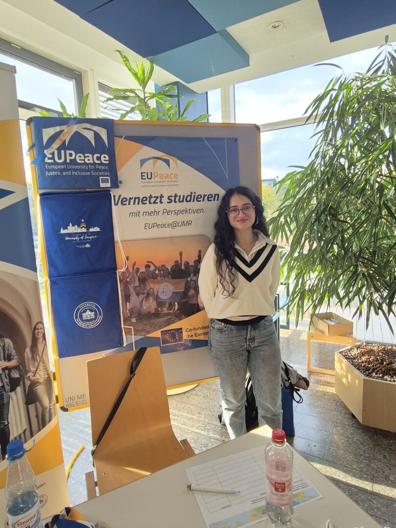 A female student assistant stands at the EUPeace Info booth at the Study Abroad Fair of the University of Marburg.