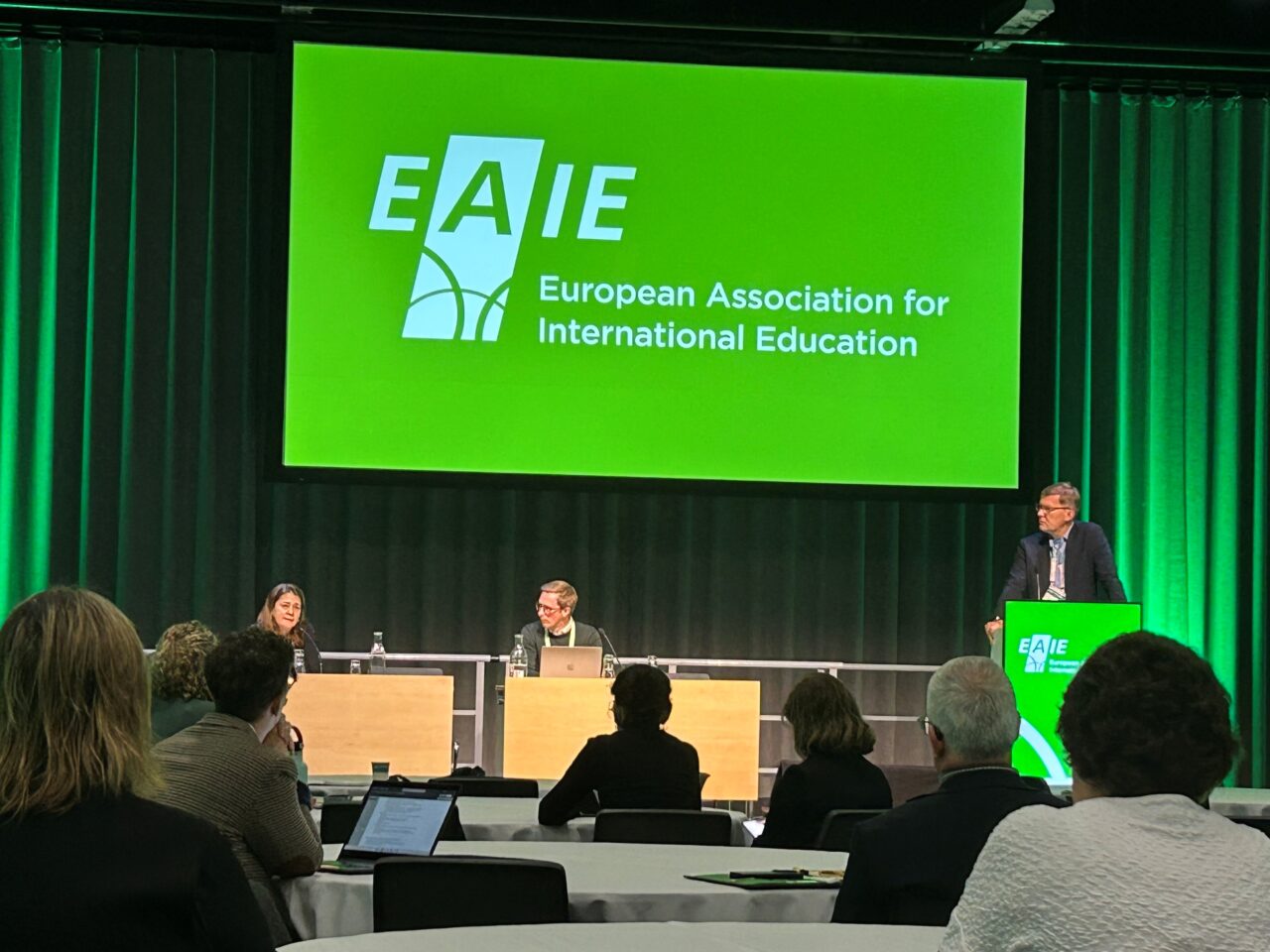 Three people on a podium at the EAIE 2025 conference. Left-to-right: Asli Ilgit (Cukurova University, Türkiye), Sebastian Kilde Westberg; University of Gothenburg & Markus Laitinen; University of Helsinki.