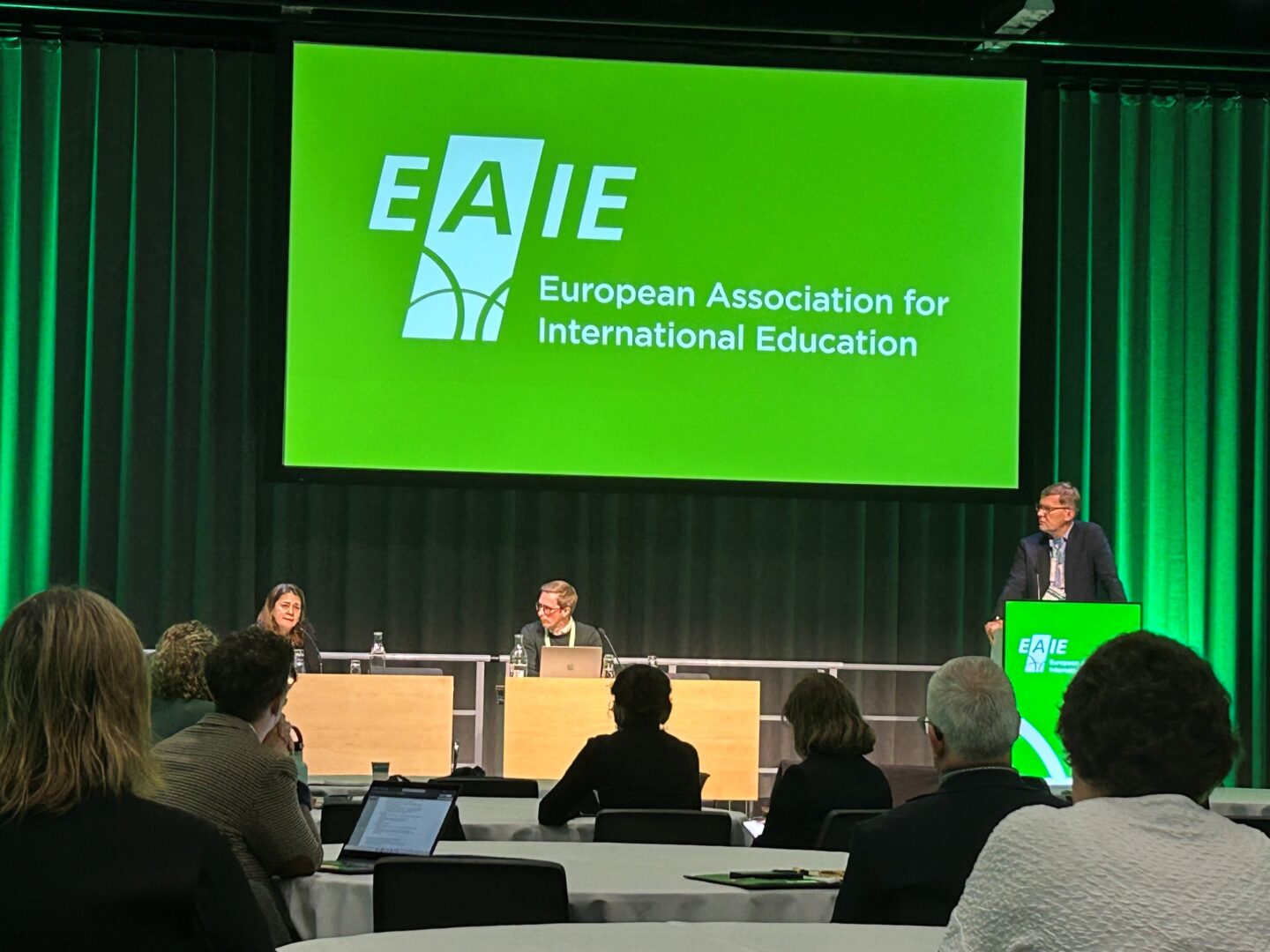 Three people on a podium at the EAIE 2025 conference. Left-to-right: Asli Ilgit (Cukurova University, Türkiye), Sebastian Kilde Westberg; University of Gothenburg & Markus Laitinen; University of Helsinki.