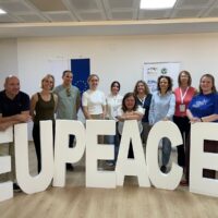 A group of people standing behind meter-high EUPeace letters.