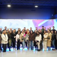 A large group of people posing in front of a large screen for a group picture. The screen shows the logo of the University of Mostar.