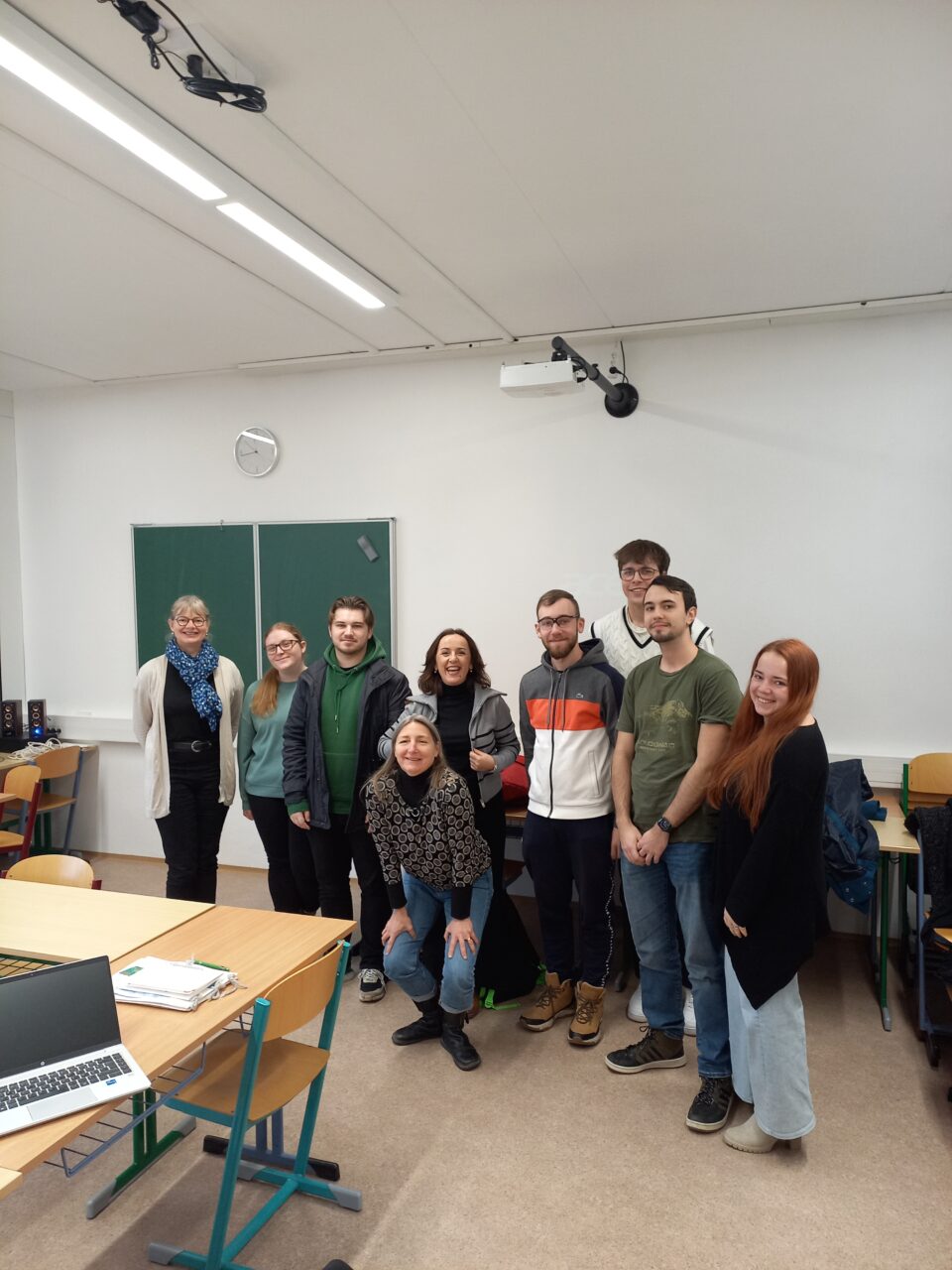 A group of nine people posing together in a classroom in front of a green chalkboard.