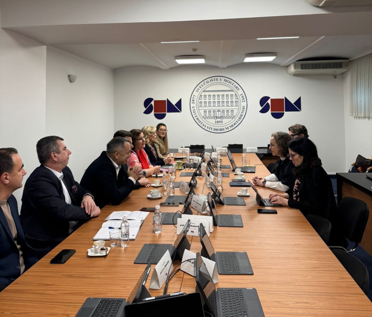 Representatives of Marburg University and the University of Mostar during a meeting at the University of Mostar. The logo of the University of Mostar is visible in the background.