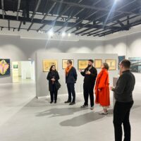 A group of five people standing in the Museum of Modern Art of the University of Mostar. Curator Dinko Baković is speaking about a piece in the exhibition Oblak u glavi.