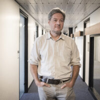 A person standing in an office hallway, hands in pockets, looking directly into the camera. The person is Pierre Mounier.