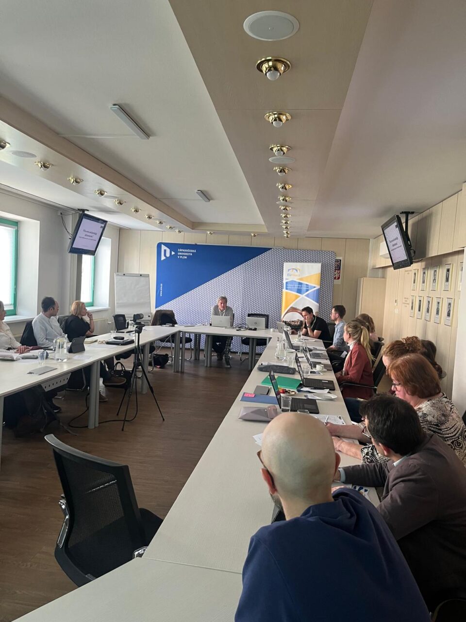 A group of people seated around tables with their laptops, listening to the keynote speaker, Pierre Mounier, at the front.