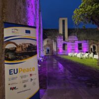 An EUPeace roll up-banner standing in the yard of an old building.