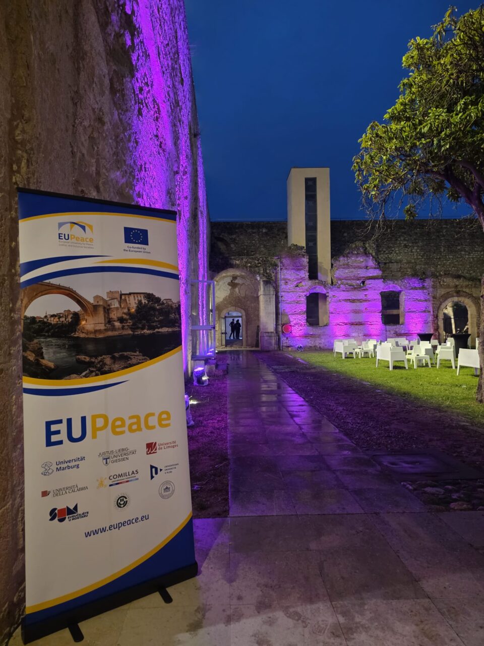 An EUPeace roll up-banner standing in the yard of an old building.
