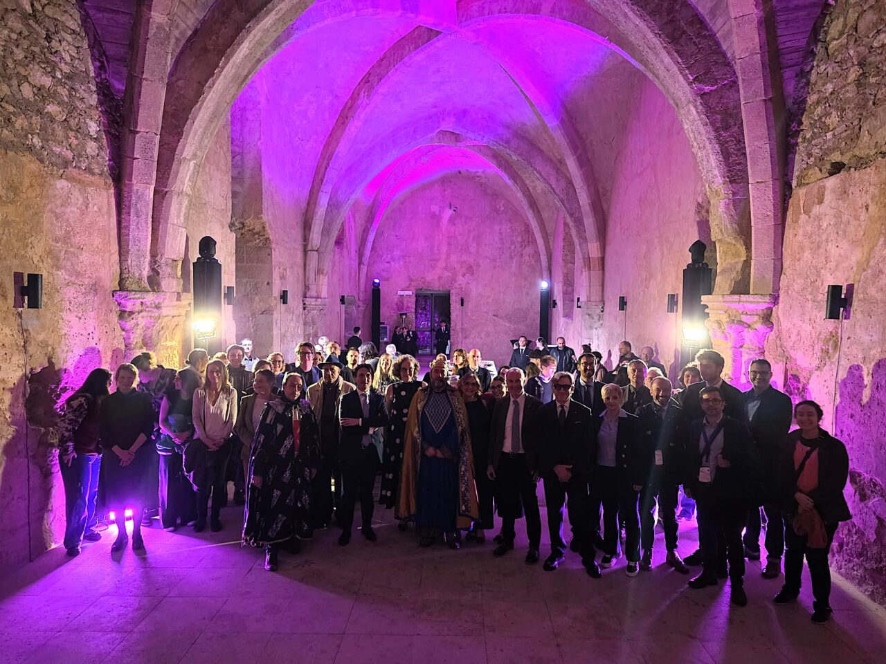 A group of people posing for a picture in an old building with an arched ceiling and purple lighting.