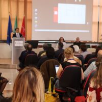 A man holding a presentation in front of an audience. The man is Gianluigi Greco.