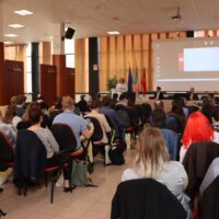 A woman holding a presentation in front of an audience. The woman is Evelyn Korn.