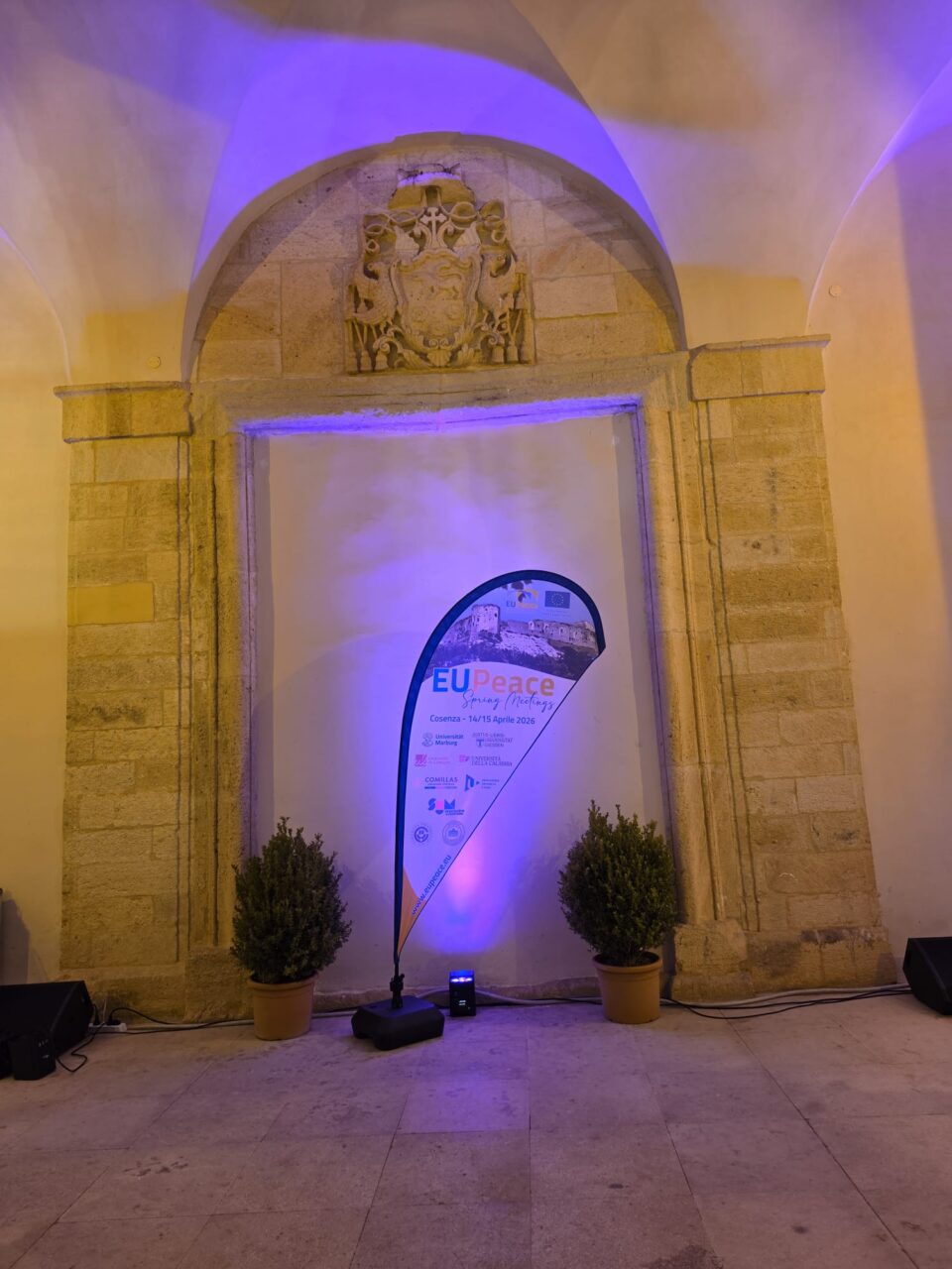 An EUPeace dropflag in front of a wall with arched ceilings, illuminated by blue lighting.