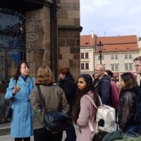 A guide in a light blue coat leads a group of EUPeace BIP participants on a city tour in front of a historic building in Pilsen, Czech Republic.