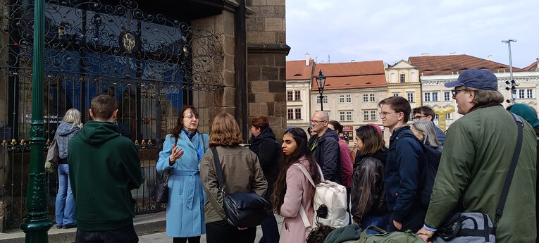 A guide in a light blue coat leads a group of EUPeace BIP participants on a city tour in front of a historic building in Pilsen, Czech Republic.