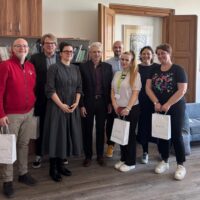 Eight EUPeace representatives pose for a group photo in an office at the Faculty of Education, University of West Bohemia in Pilsen, some holding white gift bags.