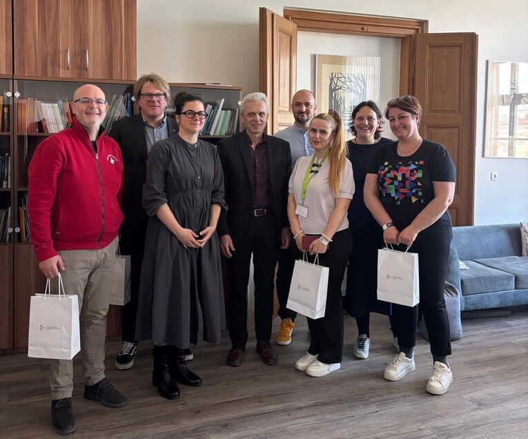Eight EUPeace representatives pose for a group photo in an office at the Faculty of Education, University of West Bohemia in Pilsen, some holding white gift bags.