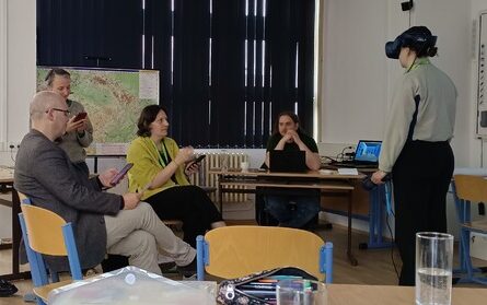 A participant tries on a virtual reality headset during a practical session at a primary school in Pilsen, while other EUPeace BIP participants observe and discuss nearby.
