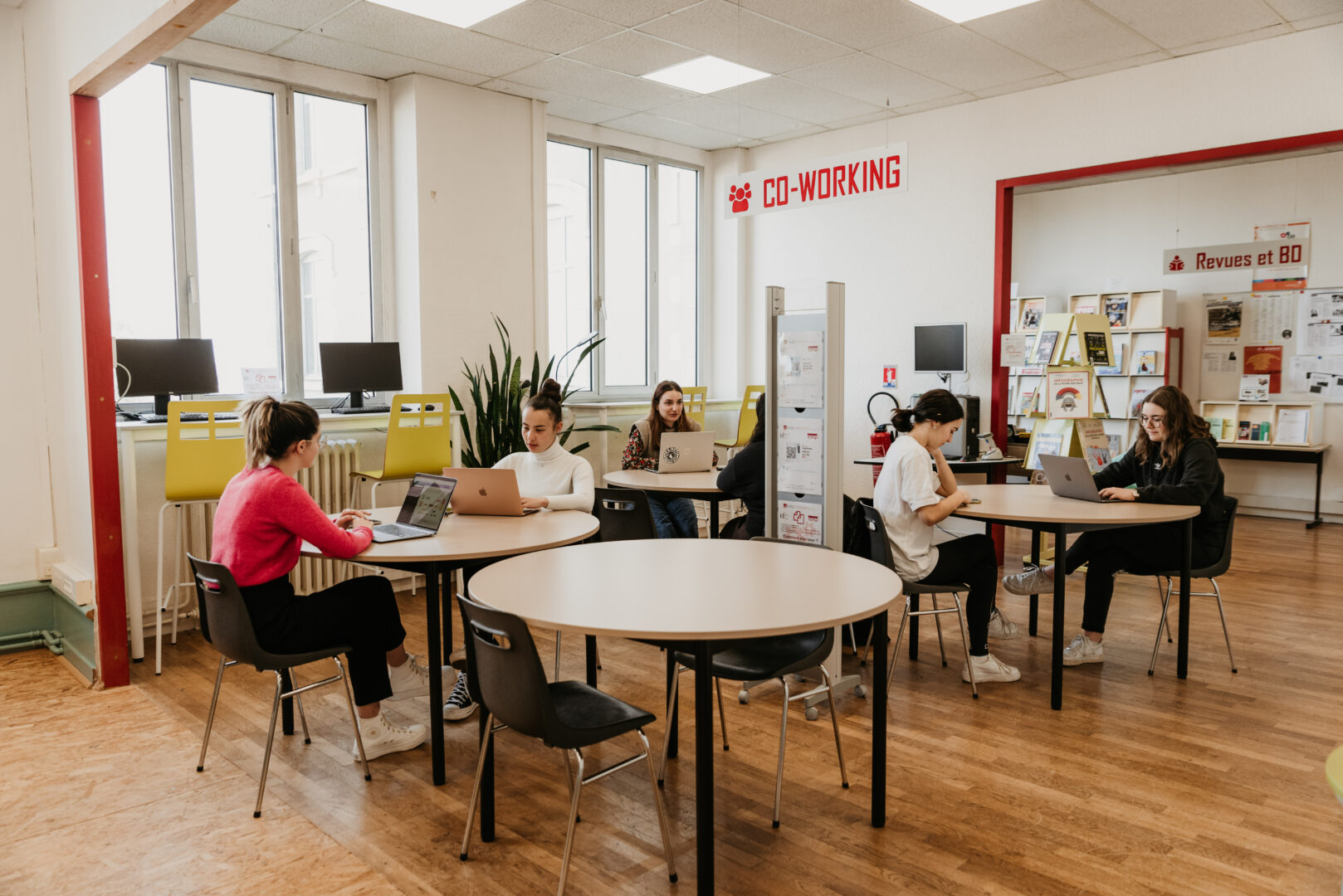 Six students sitting in front of their laptops at round tables in pairs in a co-working room at the University of Limoges.