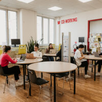 Six students sitting in front of their laptops at round tables in pairs in a co-working room at the University of Limoges.