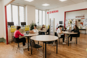 Six students sitting in front of their laptops at round tables in pairs in a co-working room at the University of Limoges.