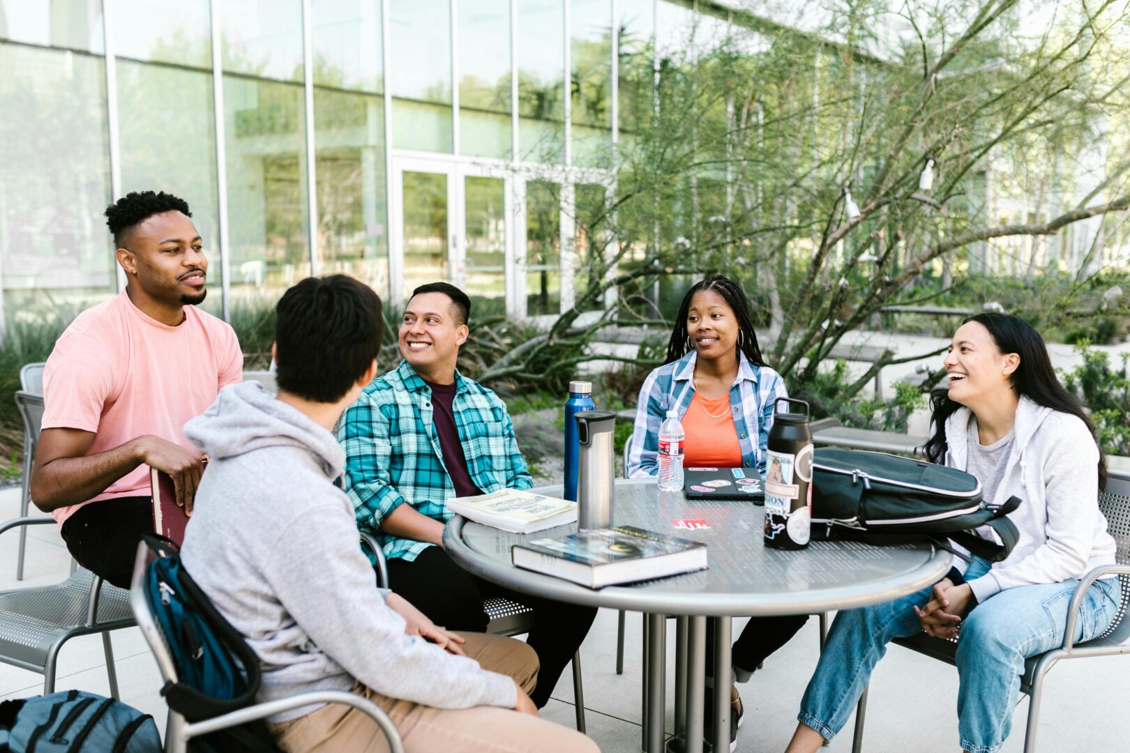 Diverse group of students sitting around a table on campus, happily conversing with each other.
