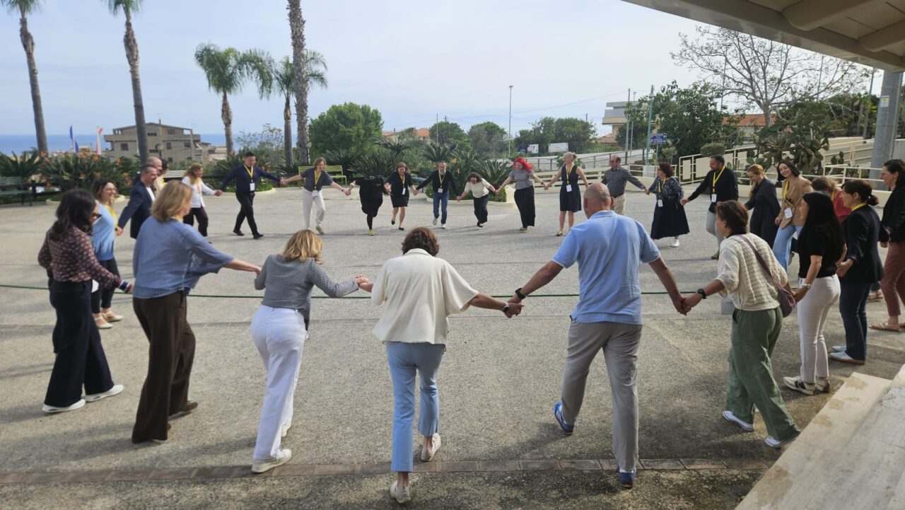 A large group of people participating in a shrinking circle activity in Tropea, Italy.
