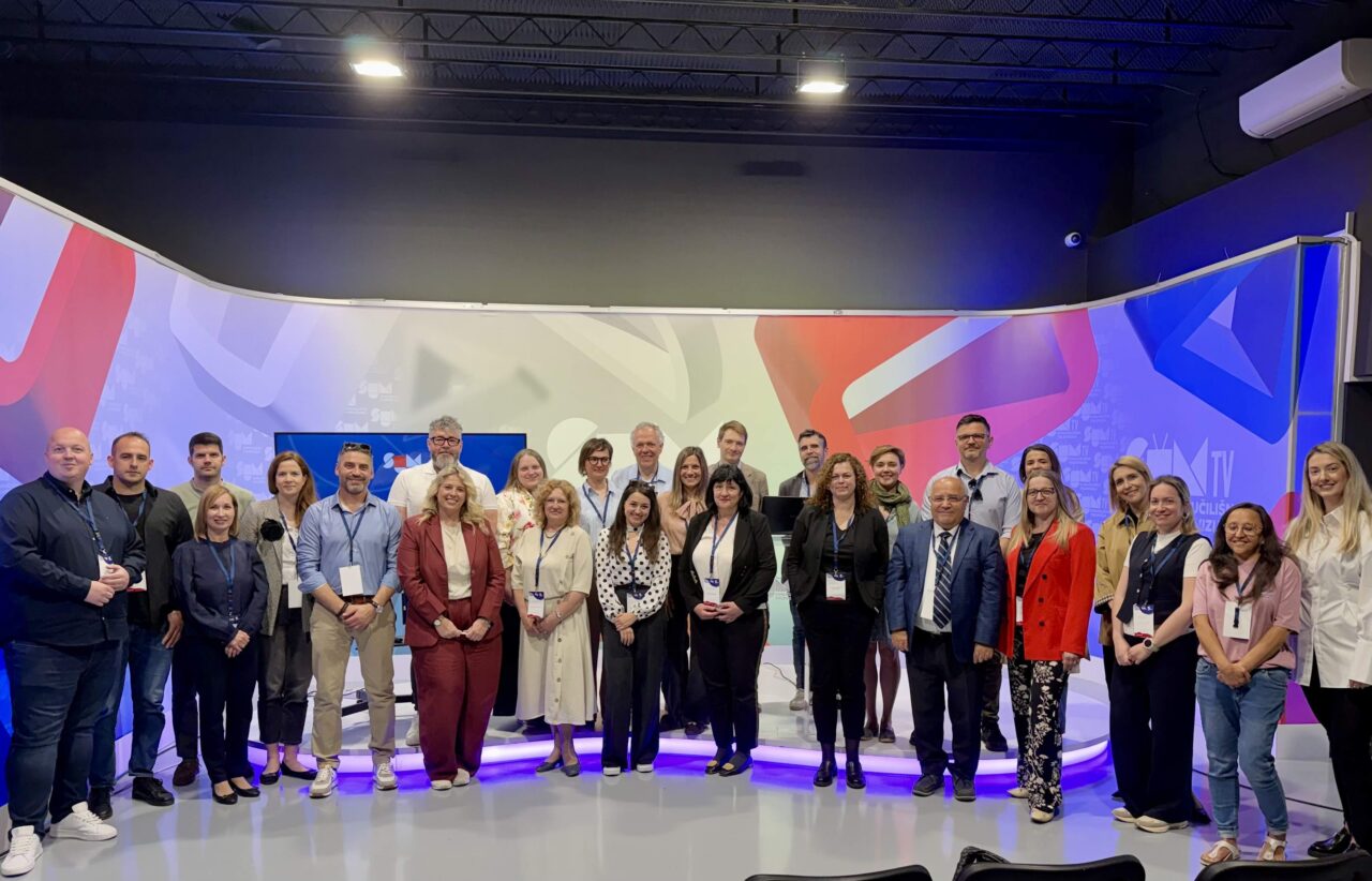 A group of 30 participants posing for a group photo in front of a big screen showing the "SUM TV" logo.