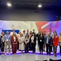 A group of 30 participants posing for a group photo in front of a big screen showing the "SUM TV" logo.