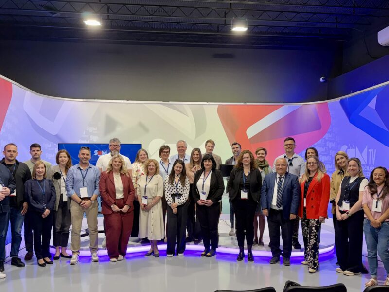 A group of 30 participants posing for a group photo in front of a big screen showing the "SUM TV" logo.