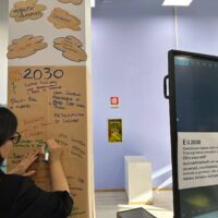 A person writing on a poster hanging on a pillar with "2030" written on the top.