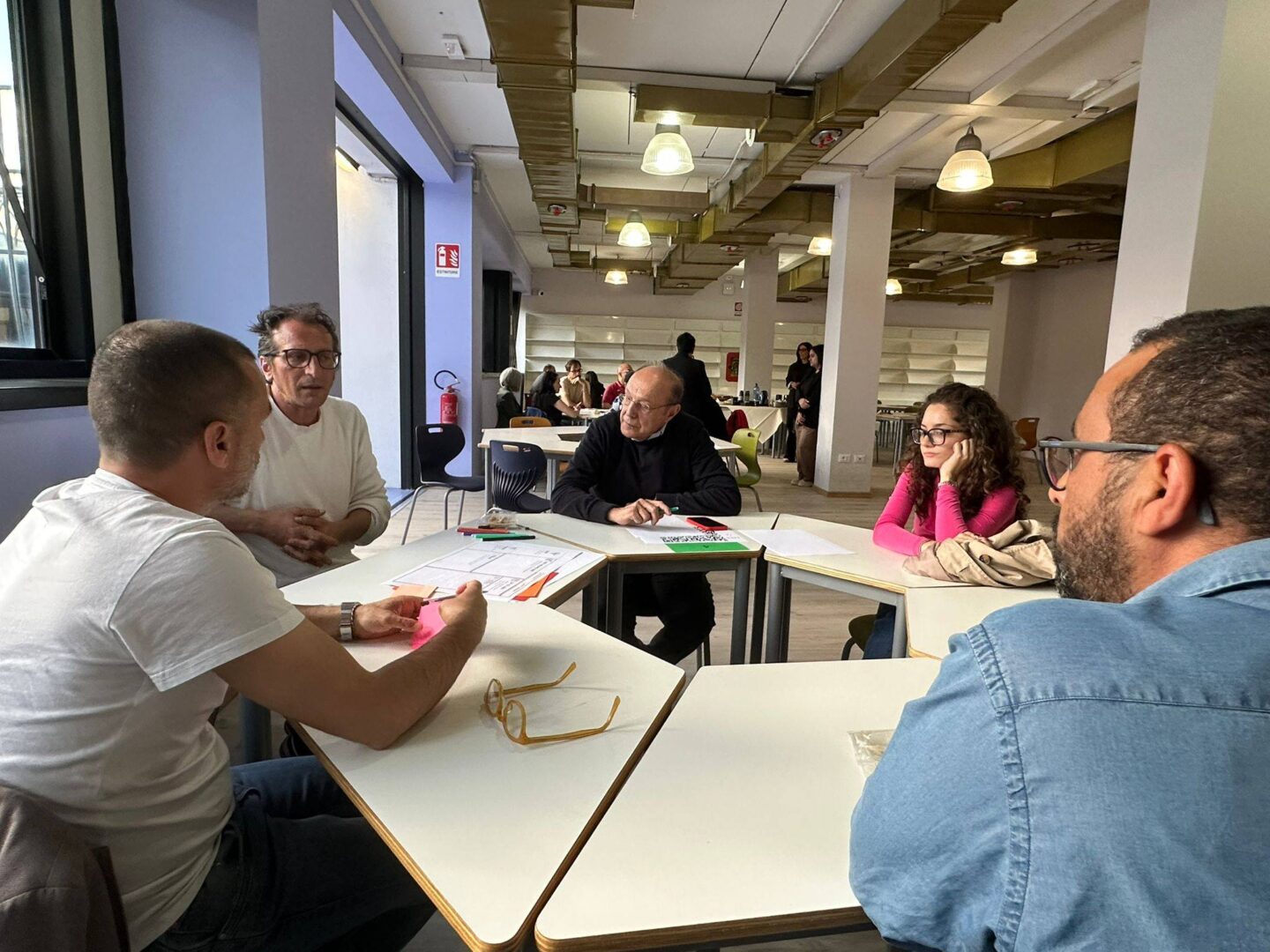 Participants attending the EUPeace Bridge Dialogue and Living Lab session at the University of Calabria during the Frontiere Festival. They are sitting in the groups around tables and conversating.