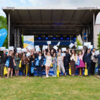 A group of students and staff in front of a stage posing for a group photo, holding their EUTrack Certificates in the air.