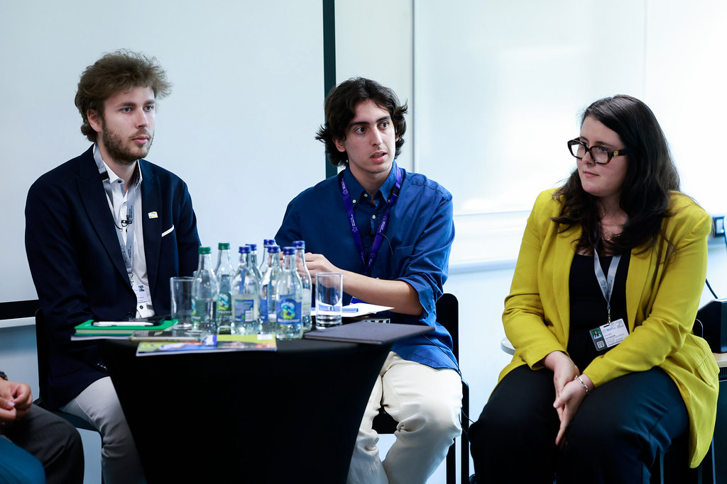 Three of the panellists sitting on high chairs around a round table, listening to someone out of frame. One of the panellists is Leon Hebeisen, Vice-President of the EUPeace Student Council.
