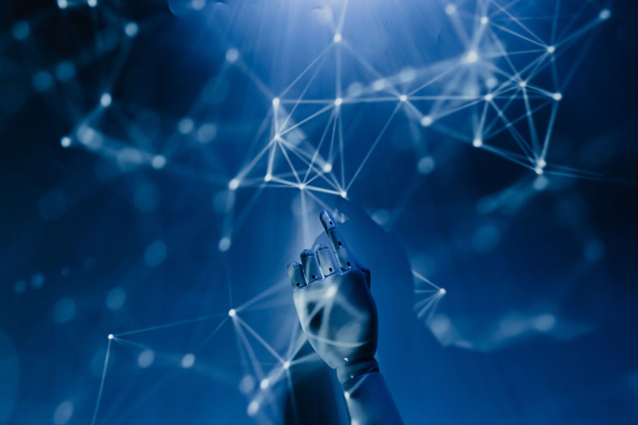 An artificial hand pointing to a network of white nodes projected onto a blue background.