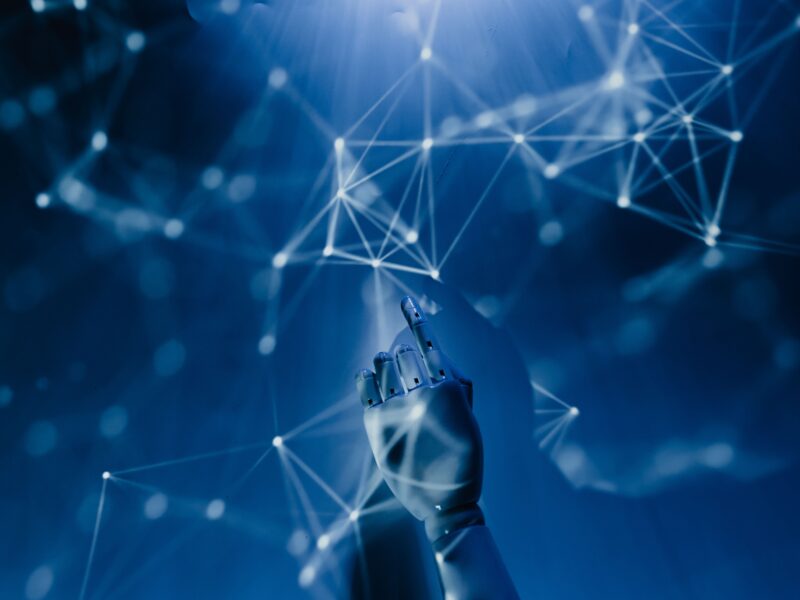 An artificial hand pointing to a network of white nodes projected onto a blue background.