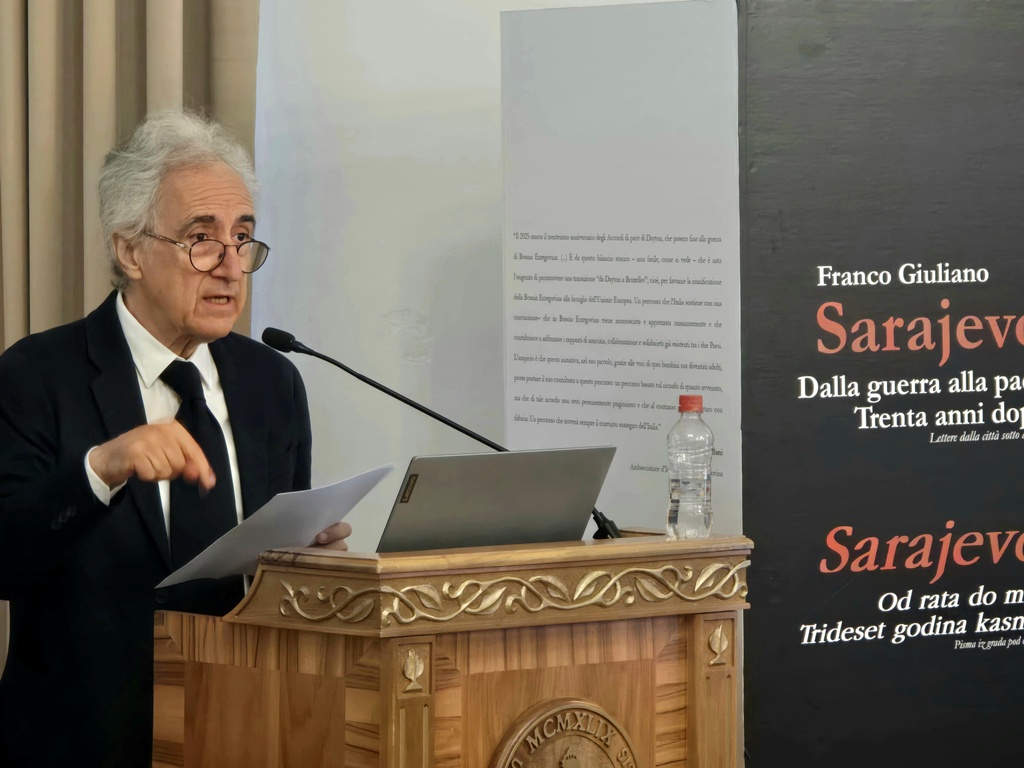 A person standing behind a podium, speaking into the microphone. The person is Franco Giuliano.