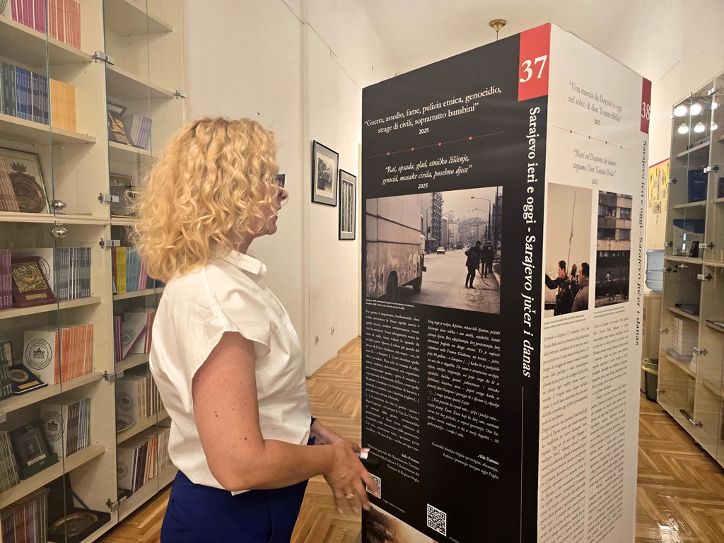 A woman standing in front of an information pillar from the exhibition, looking at the text and images.