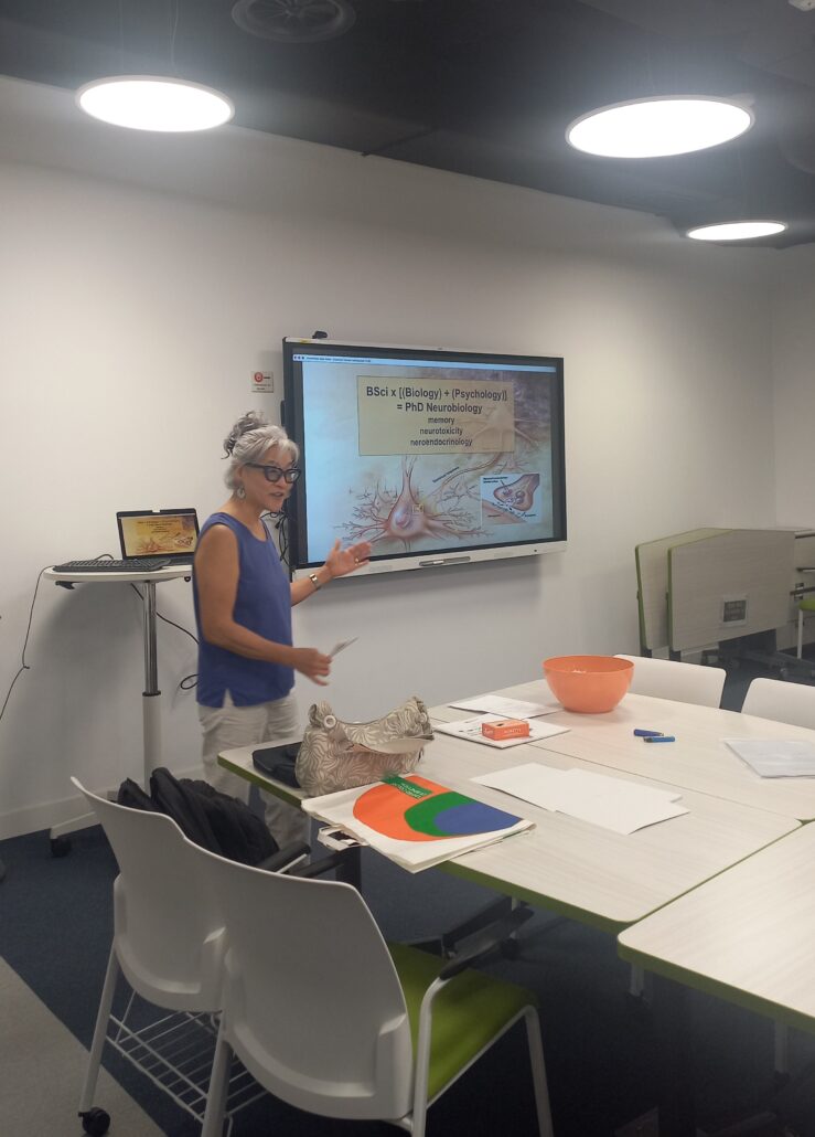 Teresa Ting speaking beside a screen showing a neuron diagram and her academic background in neurobiology.