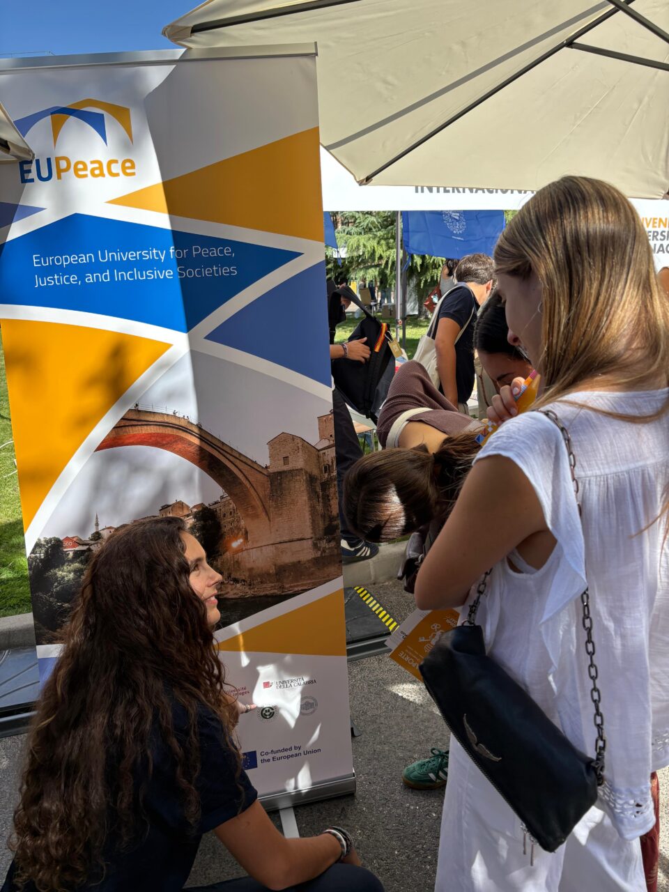 A member of the EUPeace Student Club speaks with incoming students beside the EUPeace banner.
