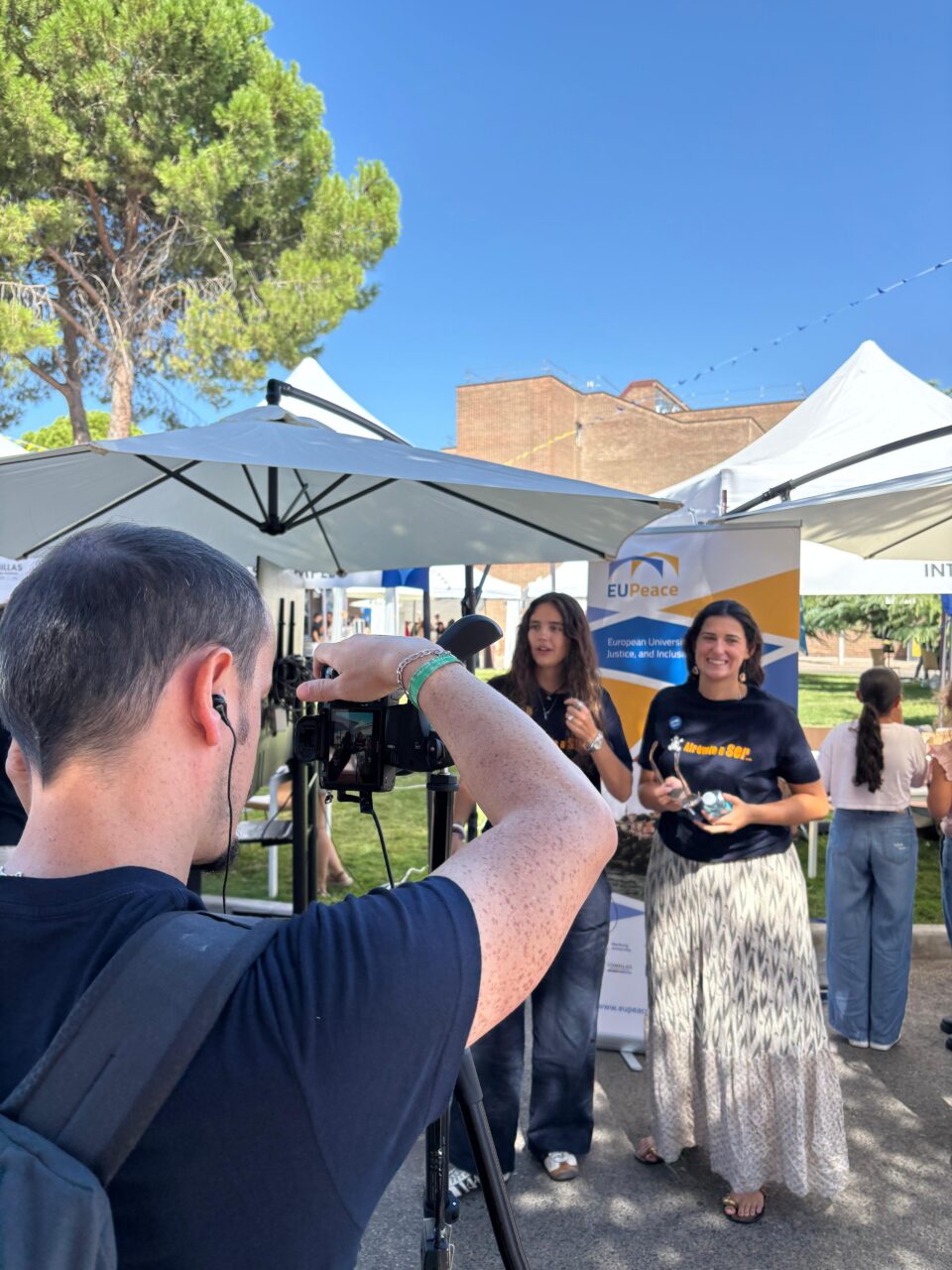 A videographer records members of the EUPeace Comillas team in front of the EUPeace stand during Welcome Day.