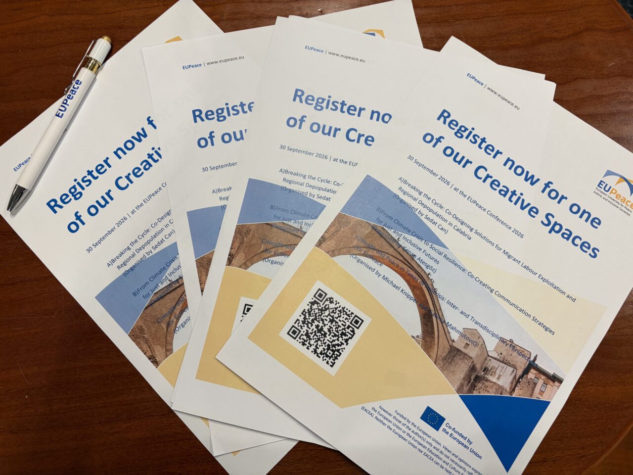 Several printed flyers fanned out on a wooden table, next to a white pen with the EUPeace logo. The flyers read "Register now for one of our Creative Spaces – 30 September 2026 at the EUPeace Conference 2026" and list three sessions: "Breaking the Cycle", organised by Sedat Can; "From Climate Crisis to Social Resilience", organised by Kenan Ateşgöz; and "Health and Peace in Times of Polycrisis", organised by Michael Knipper and Fatima Mahmutović. Each flyer shows a QR code, a photo of the Old Bridge in Mostar and the "Co-funded by the European Union" emblem.